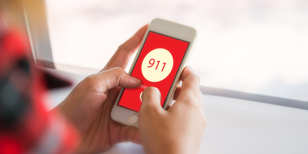 Konvoy Person Dialing 911 Person holding a smartphone with a red screen displaying "911" and an emergency call button.