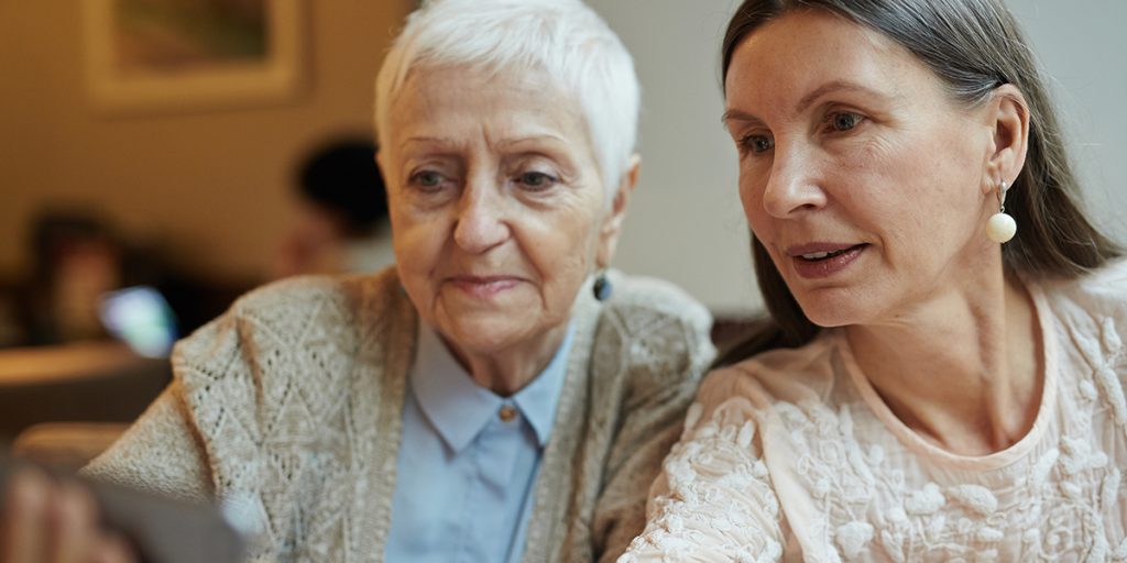 Two women, one older and one middle-aged, sit closely together looking at something off-camera.