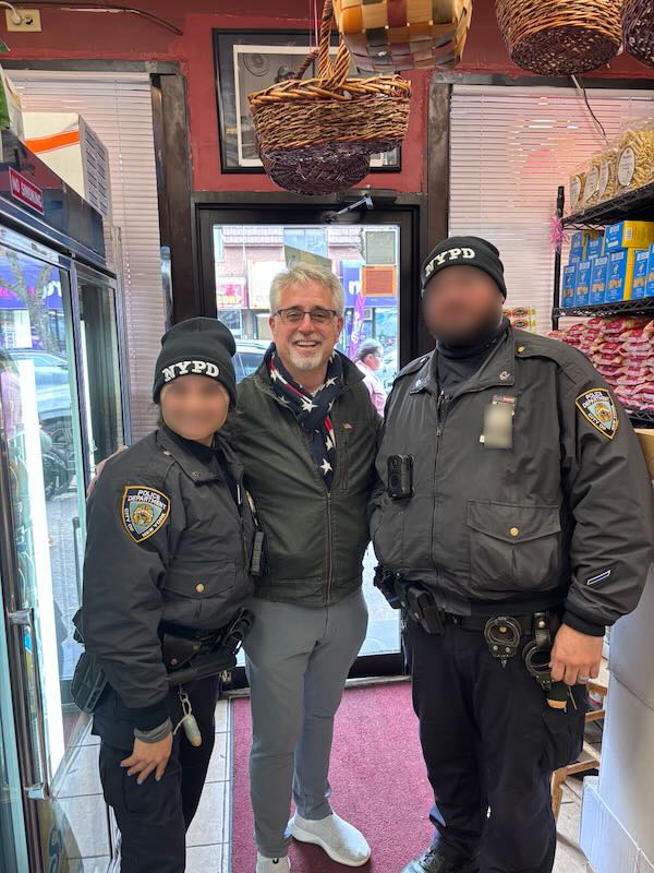 A smiling man standing between two NYPD officers in a shop.